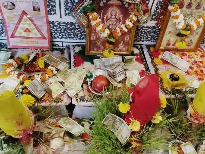 Hindu altar with deity images, flowers, and money offerings during a religious ritual.