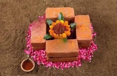 Flower arrangement placed on bricks, surrounded by petals and a small oil lamp on soil.