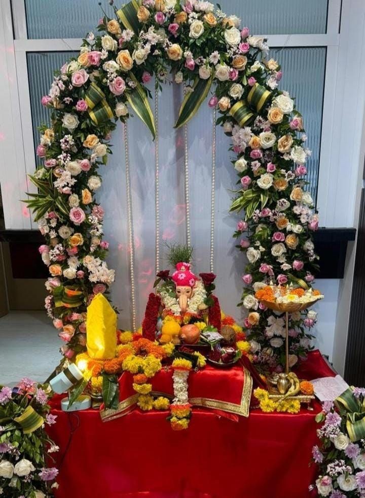 Floral arch with an adorned deity idol surrounded by garlands and offerings on a decorated table.