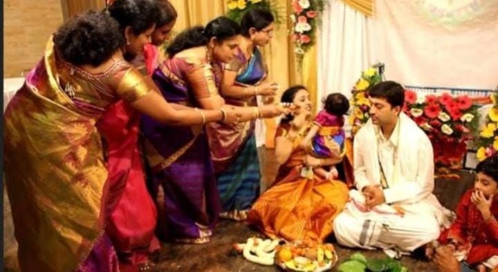 A group of people in traditional attire participating in a cultural ceremony with colorful floral decorations and offerings.