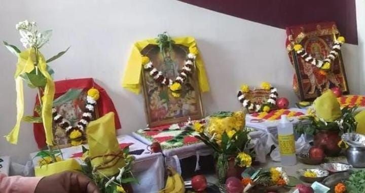 Indian religious altar with framed deities, flowers, and ritual items on a table.